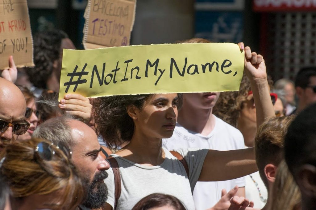 Woman holding a sign with the hashtag "NotInMyName" in Las Ramblas memorial. Photo by: Evan McCaffrey