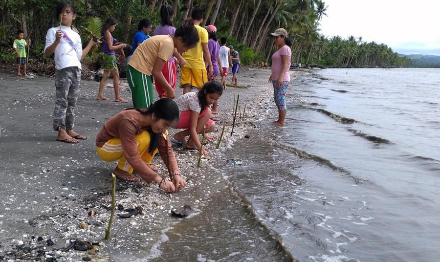 Plan International Filipino activist, Louisa (in brown) planting mangrove seedlings on a beach to disaster-proof her communities. Photo by: courtesy Plan International.